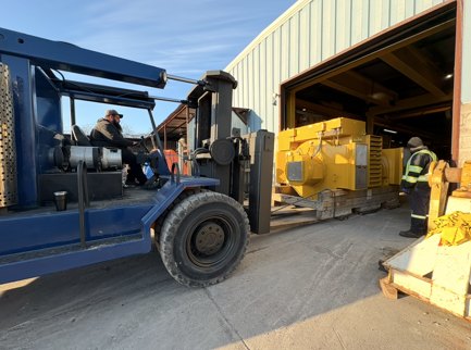 Industrial forklift and machinery secured on a flatbed outside a facility