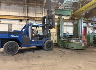 Heavy industrial forklift moving a large machine in a factory