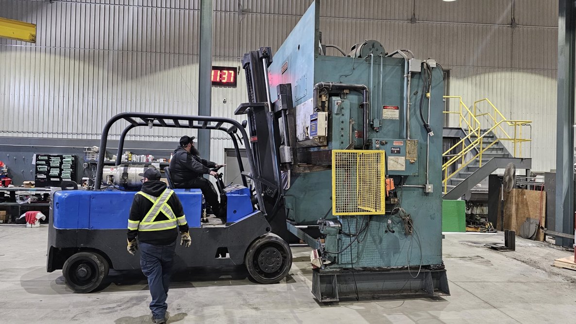 Large industrial machine being moved with a yellow forklift inside a workshop